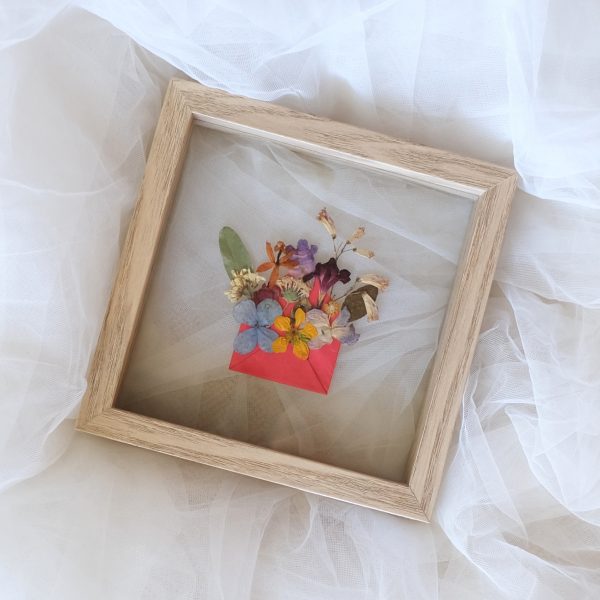Pressed Flower Art Blossom Mail featuring flowers popping out from a mini red envelope and framed in a double glass wooden frame which lays on a tulle fabric